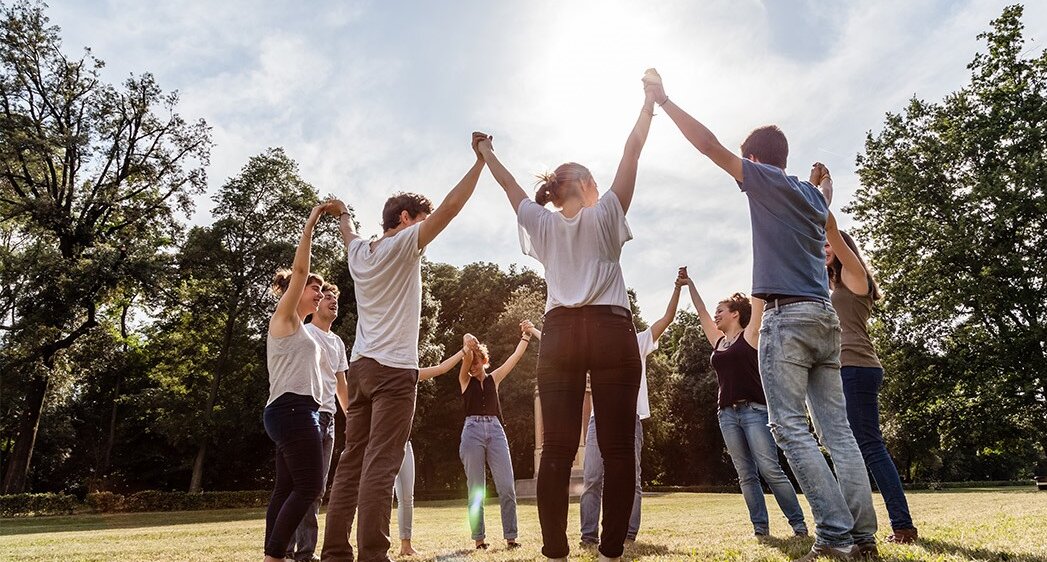 Eine Gruppe von Jugendlichen steht draußen im Kreis zusammen und sie halten ihre Hände nach oben | © iStock.com/lorenzoantonucci